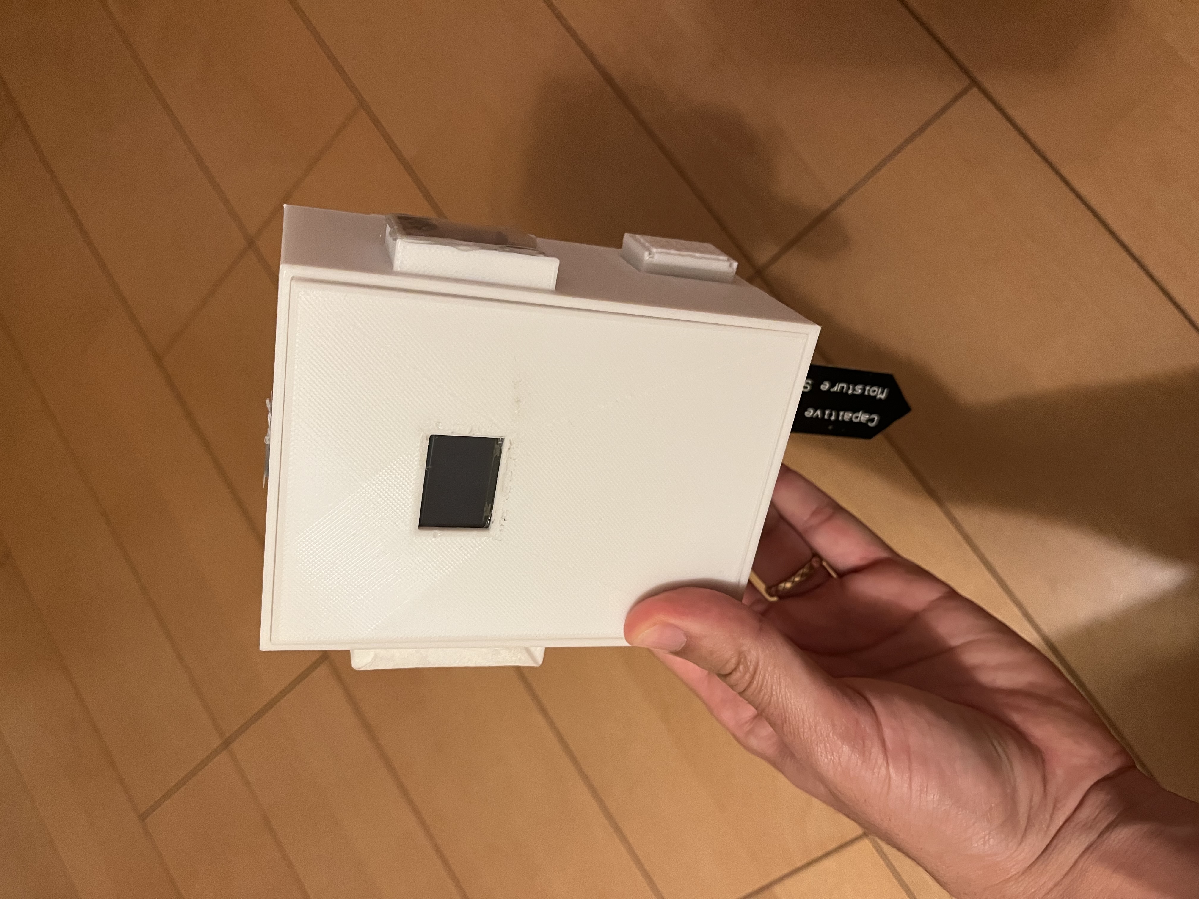 A handheld Talking Plants sensor device in a white enclosure with a small display